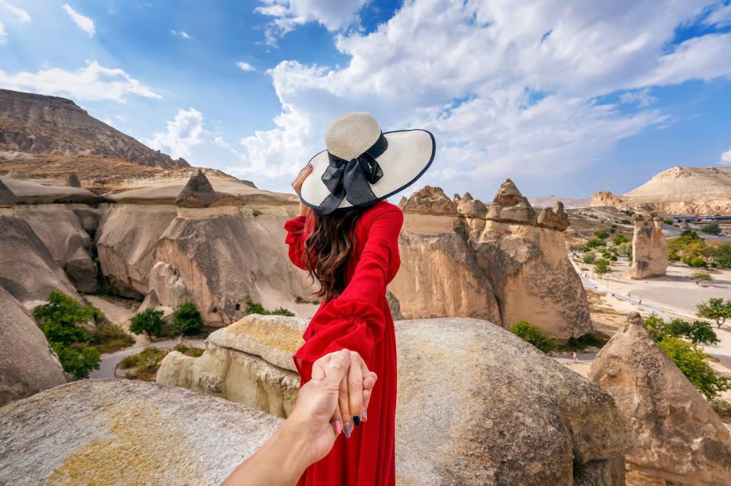Guest in a red dress holding a hand toward Cappadocia fairy chimneys on the bookable Cappadocia Red Tour from The Owl Cave Hotel, Göreme